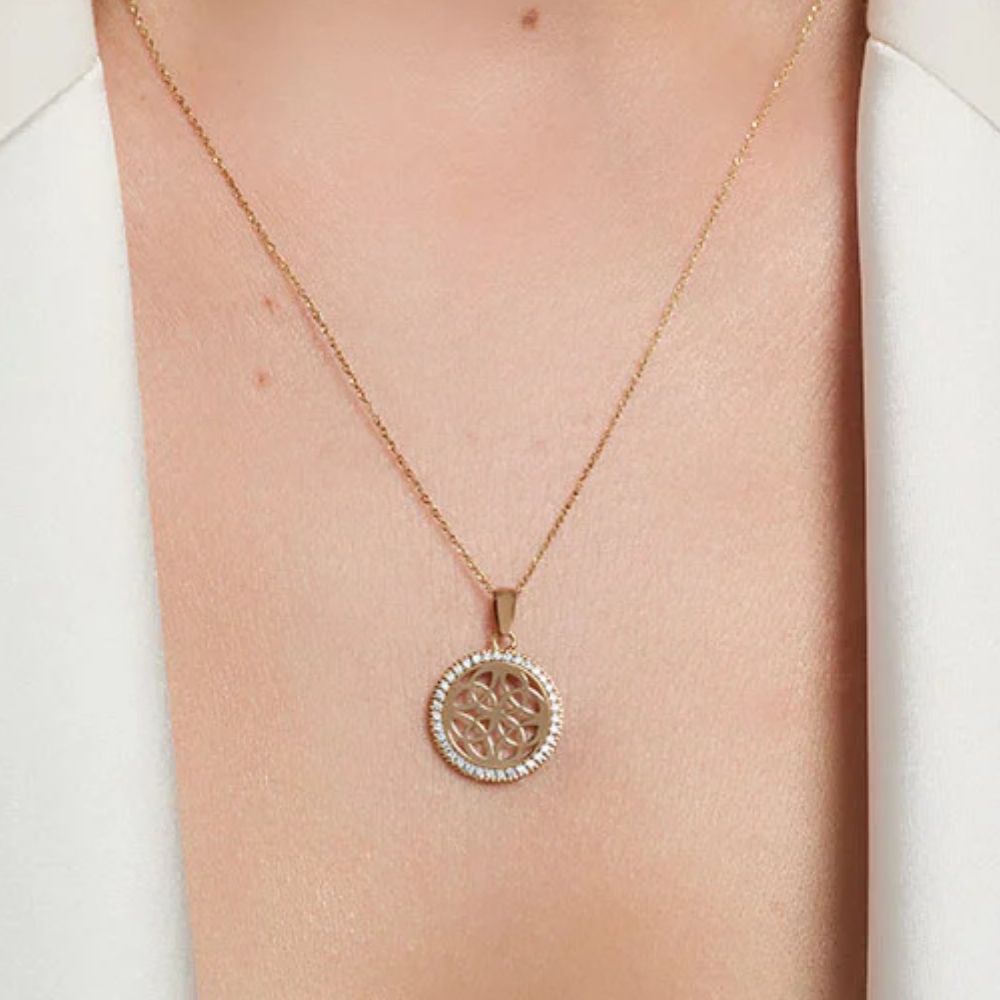 Rose gold necklace with a circular pendant on a person wearing a white top.