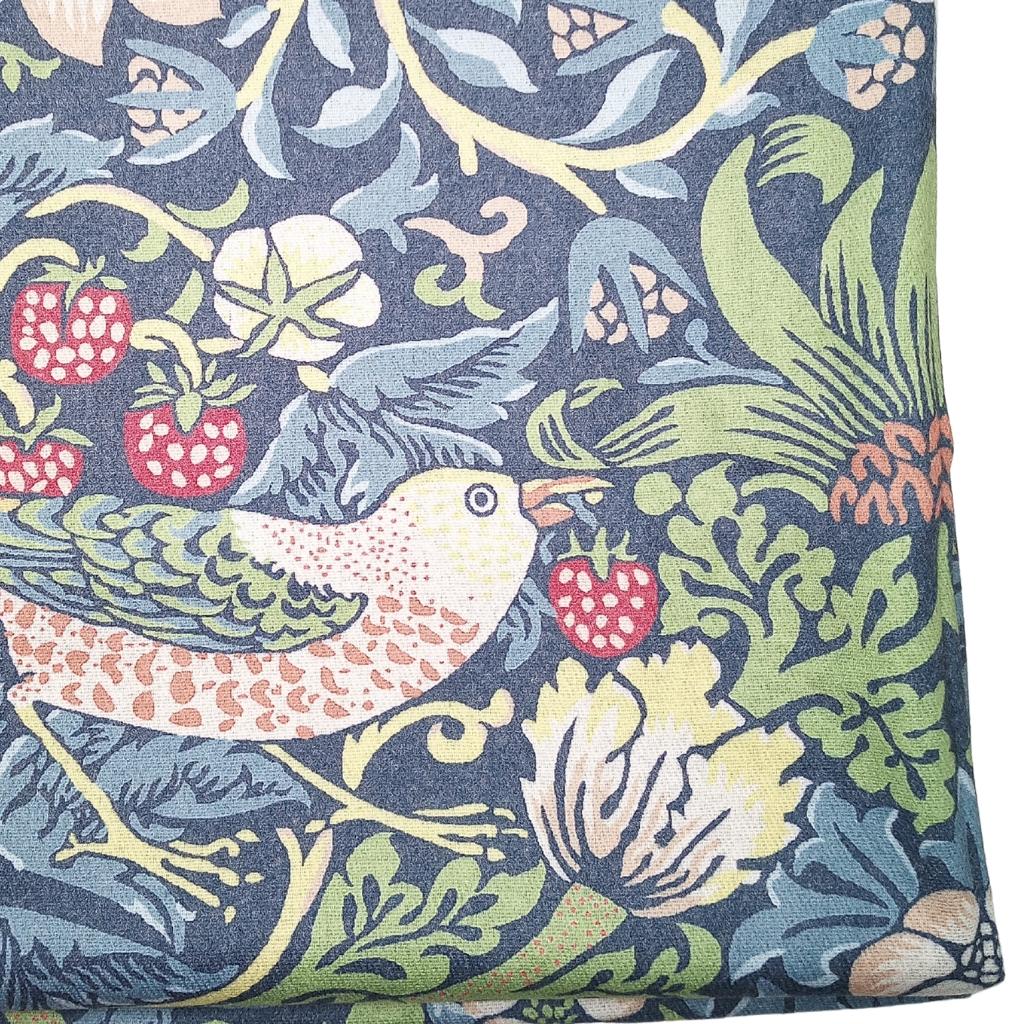 A close-up of a fabric product featuring a classic William Morris-style botanical and bird pattern. The design includes a detailed bird in green, pink, and white, surrounded by red berries, green leaves, and cream flowers on a dark navy blue background.