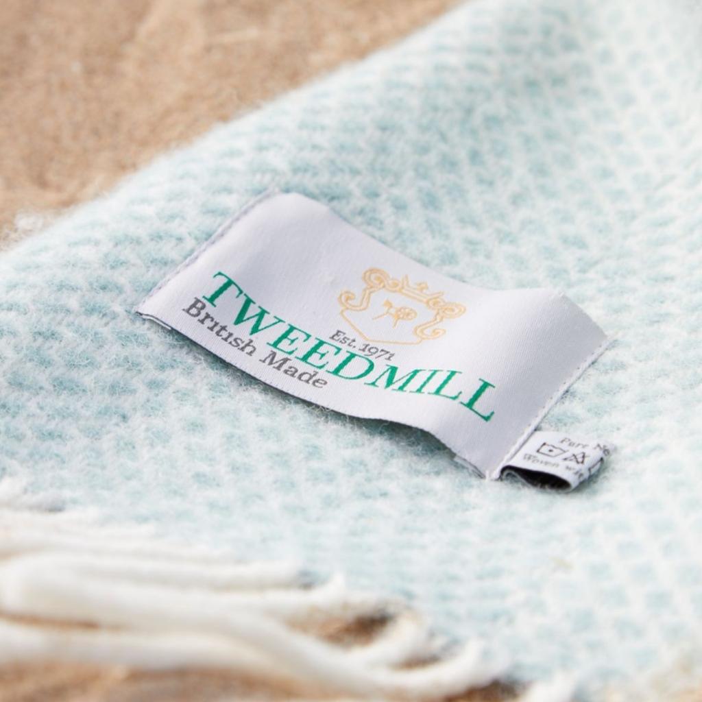 Close-up of Tweedmill Beehive Ocean wool throw label on a soft ocean-colored weave.