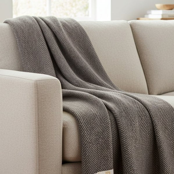 A folded gray and beige herringbone woven throw blanket with cream fringe and a small white brand tag, shown on a plain white background.